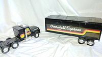 Front side view of the black semi truck and trailer showing Overnight Express markings and colorful stripes on both pieces.