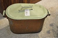Photo showing antique copper bin with an oval, light green painted lid featuring a handle. Two side handles on bin body visible. Copper surface shows age wear.