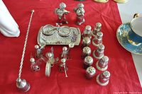 Top-down photo showing a collection of assorted salt and pepper shakers, including metal, glass, decorative angels, and ceramic tray with shakers on a red cloth.