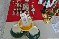 Four assorted vintage teacups with matching saucers displayed on a red tablecloth including a yellow/gold cup and green embossed cups.