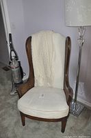 Full view of the tall wingback chair with cream upholstery and knitted blanket draped over it, showing the wooden frame and seat.