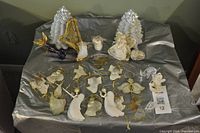 Photo of white and gold Christmas decorations including angel figurines, ornaments with gold strings, and decorative items arranged on silver fabric.