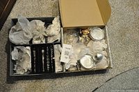 Overhead view of two open boxes containing various glass Christmas ornaments wrapped in white tissue paper.