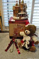 Entire lot displayed on countertop: Gingermint House box underneath decorative house, plush bear beside two red metal hangers