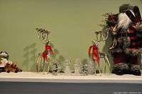 Wide shot showing Santa Claus figures, silver reindeer candle holders with red bows, clear acrylic Christmas trees and angels.