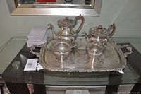 Photo taken showing full coffee and tea set arranged on large serving tray on a glass table with reflection visible