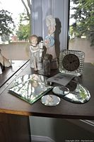 Photo of glass clock, mirror trivet pieces, and assorted angel figurines on wooden table by window with outdoor view.