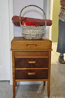 Closed antique wooden sewing cabinet with woven basket and fabric roll on top