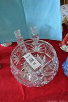 Clear crystal bowl and two crystal candle sticks placed on a red surface with light blue background cloth.
