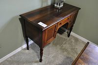 Side angled view showing wooden desk's finish, drawer, legs, and cabinet door.