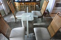 Front angle view of square glass top dining table with marble base and surrounding chairs not included in lot