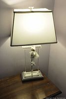 Table lamp with rectangular shade lit, sitting on a wooden surface next to a chair.