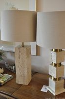 Pair of table lamps: left - rectangular travertine block lamp; right - stacked travertine cube lamp with brass accents, both with beige fabric drum shades