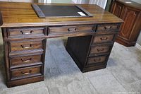 Front view of the large wooden office desk showing top surface with leather pad and drawers.