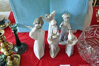 Five Lladro porcelain figurines displayed together on a red cloth with some other decorative items partially visible.