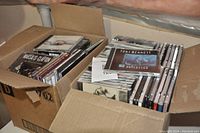 Two cardboard boxes filled with jewel case music CDs, with visible titles including Tony Bennett and Eric Clapton albums.