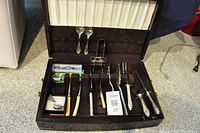 Brown case containing multiple assorted serving utensils and cutlery held in place with compartments and clips