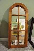 Antique oval top wooden framed mirror with grid dividing the mirror glass into six sections, shown standing against a wall.