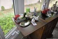 View of a collection of miscellaneous bird figurines and other decorative items placed on a wooden surface near a window showing natural light and outdoor greenery