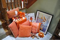 Overall view showing five different orange pillows, two pieces of framed artwork, and some decorative items at the base of stairs.