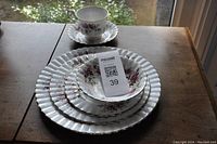 Stack of Royal Albert Lavender Rose china including fruit bowl, salad plate, dinner plate, bread plate, and saucer with teacup on top, showing floral rose pattern and gold trim on white china.