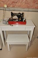 Singer sewing machine with table and stool on a white table against a basement wall.