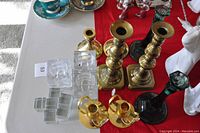 Top view showing collection of brass and green glass candle sticks grouped with clear acrylic table card holders on table with red runner