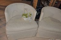 Pair of white fabric barrel chairs with one carrying a small white basket with artificial succulent plants