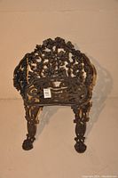 Full view of wrought iron outdoor chair showing ornate floral and grapevine design on backrest and seat area, claw-foot legs visible.