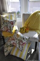 Two cream upholstered accent chairs with dark wooden legs, one draped with a yellow throw, both featuring a mix of floral and yellow striped cushions.