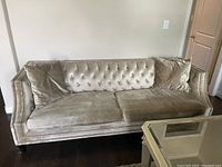 Front and side view of champagne velvet sofa with tufted back and nailhead trim, includes two large seat cushions and matching throw pillows.