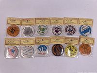 Top-down view of 12 vintage Badge-A-Minit button pins still sealed in original packaging showing variety of designs and slogans.