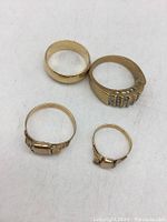 Top view of 4 vintage gold tone rings showing two plain bands and two ornate rings with faux stones.