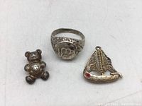 Photo showing silver textured ring, silver bear pendant with diamond, and gold-toned yacht pendant with red stone.