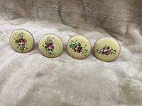 Four wooden tie backs with hand-painted floral designs arranged in a row on a fabric surface.