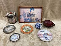 Photo showing all 8 Asian decorative items with dragon ware pieces, tray, plates, teapot, and candy dish on beige fabric.