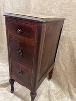 Front side angled view of antique wooden side table showing three drawers with metal knobs and turned legs.
