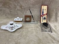 Two photos showing two fountain pen sets including ceramic inkwell with matching blotter, glass inkwell, a desk clock with pen holder on marble base, and fountain pen in original packaging.