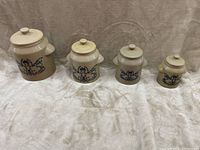 Photo showing four graduated ceramic pottery canisters with lids, beige color with blue decorative design, arranged from largest to smallest