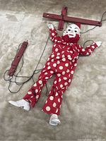 Scary clown marionette lying face up with visible wooden control bar and strings on a beige surface.