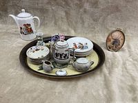 Full view of the Hummel ceramic tea set arranged on a decorative tray with multiple pieces including plates, teapot, sugar bowl, creamer, ceramic flower vase, and a framed Hummel art piece alongside a flower-shaped candle holder.