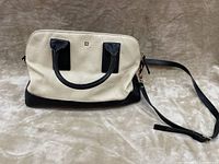 Front view of cream and black leather Kate Spade crossbody bag lying flat with handles upright and long adjustable strap extended.