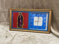 Front angled view of the large rectangular wall clock with Virgin Mary depiction and blue clock panel, showing brown gold-tone frame and attached power cord.