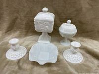 Milk glass set with two candlestick holders, one square covered piece with fruit relief, one round covered piece, and one open divided dish.