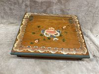 Top view of rectangular wooden lap desk closed, showing floral painted design and decorative border on top.