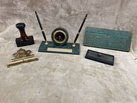 Full desk set arranged on beige cloth: marble pen stand with clock and pens, ink well, blotter, stamp, certificate holder, carrying case.