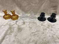 Photo showing all six candlesticks in three pairs on a beige fabric background: two amber, two clear, two black.