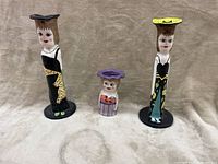 Wide shot of the three unusual ceramic woman figurine candlestick holders arranged on neutral background.