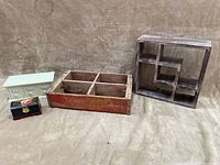 Four items displayed on a textured brown cloth background. From left to right: light green mini drawer shelf cabinet, black floral decorative chest box, vintage Coca-Cola wooden carrier with compartments, segmented dark wooden display shelf.