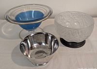 Three decorative footed bowls: one frosted glass with roses and silver-plated base, one clear glass with blue and gold decoration, and one small shiny silver-plated bowl.